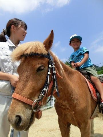 ポニーに乗馬している男の子と係りの女性の笑顔の写真